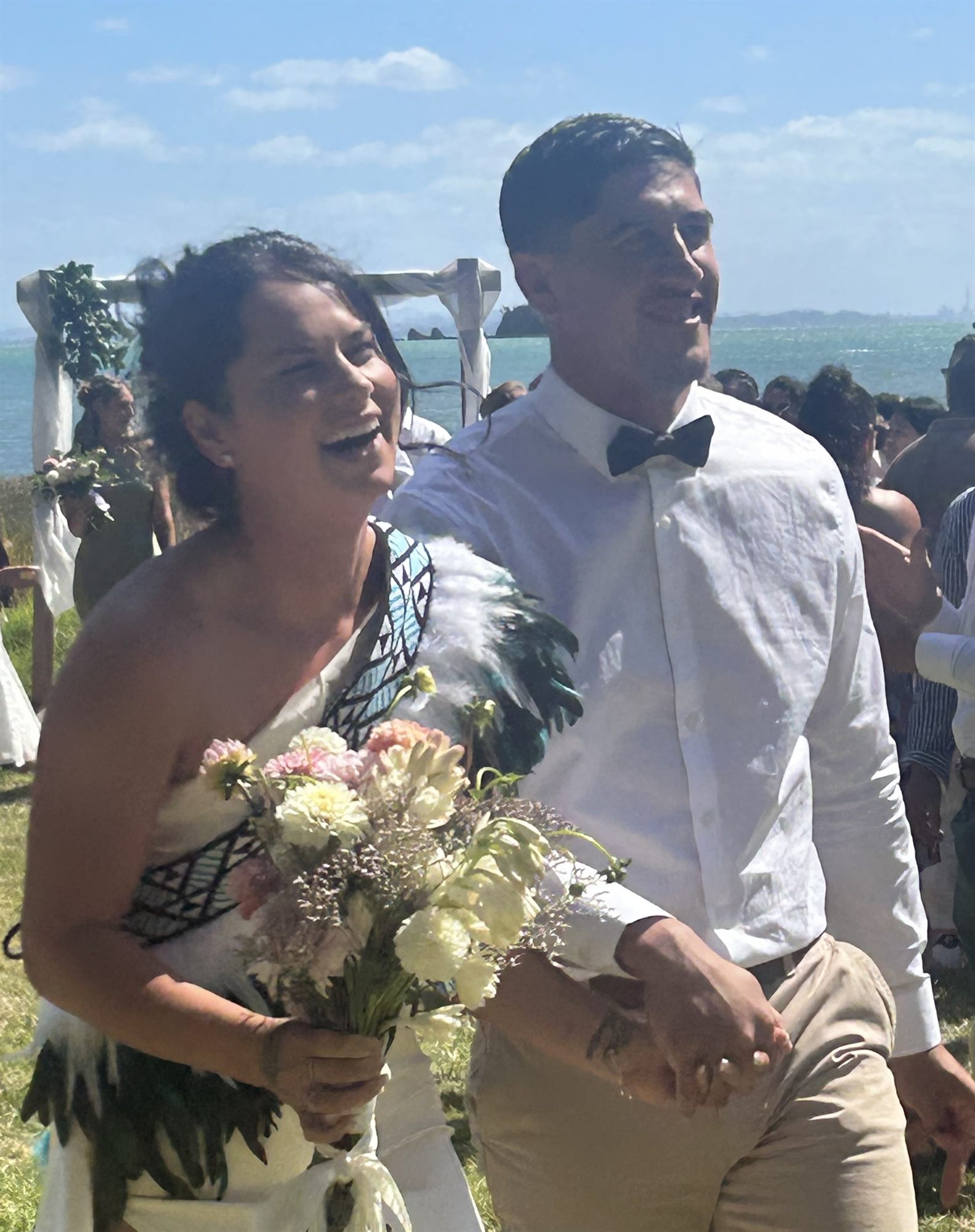 Rene and Cory joyfully walking from their wedding ceremony with Waiheke Island harbour views behind them