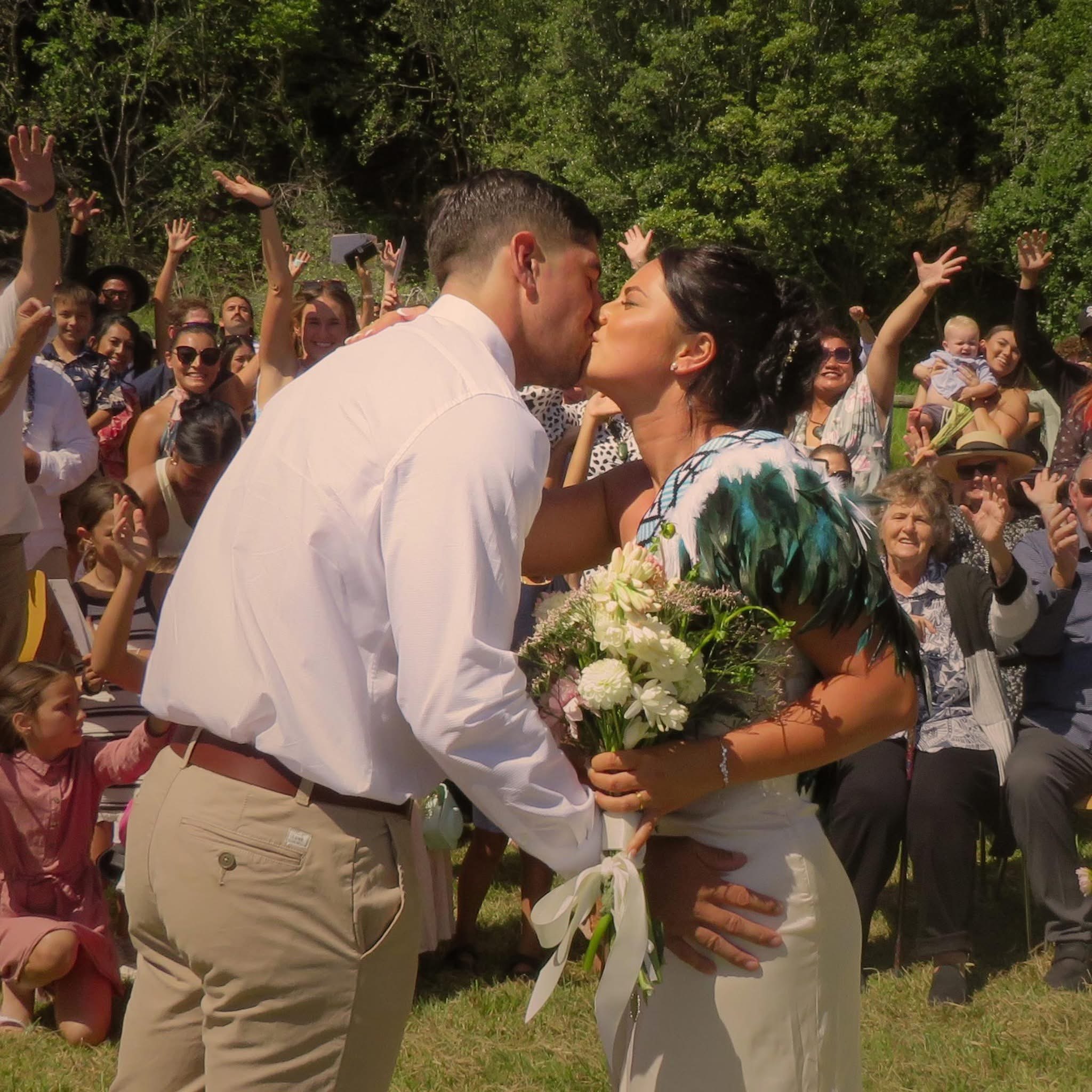 Rene and Cory sharing their first kiss as a married couple while guests cheer - Waiheke Island wedding ceremony