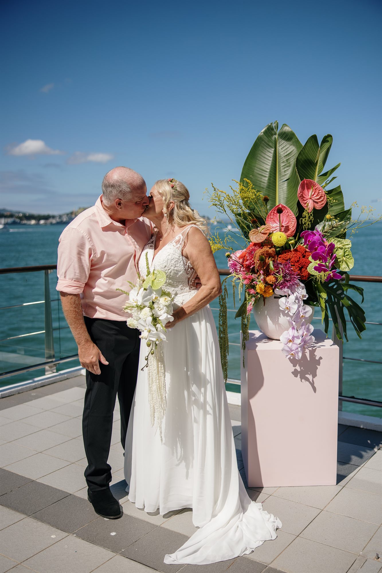 Sue and Pablo sharing their first kiss as a married couple with stunning harbour views and tropical flowers