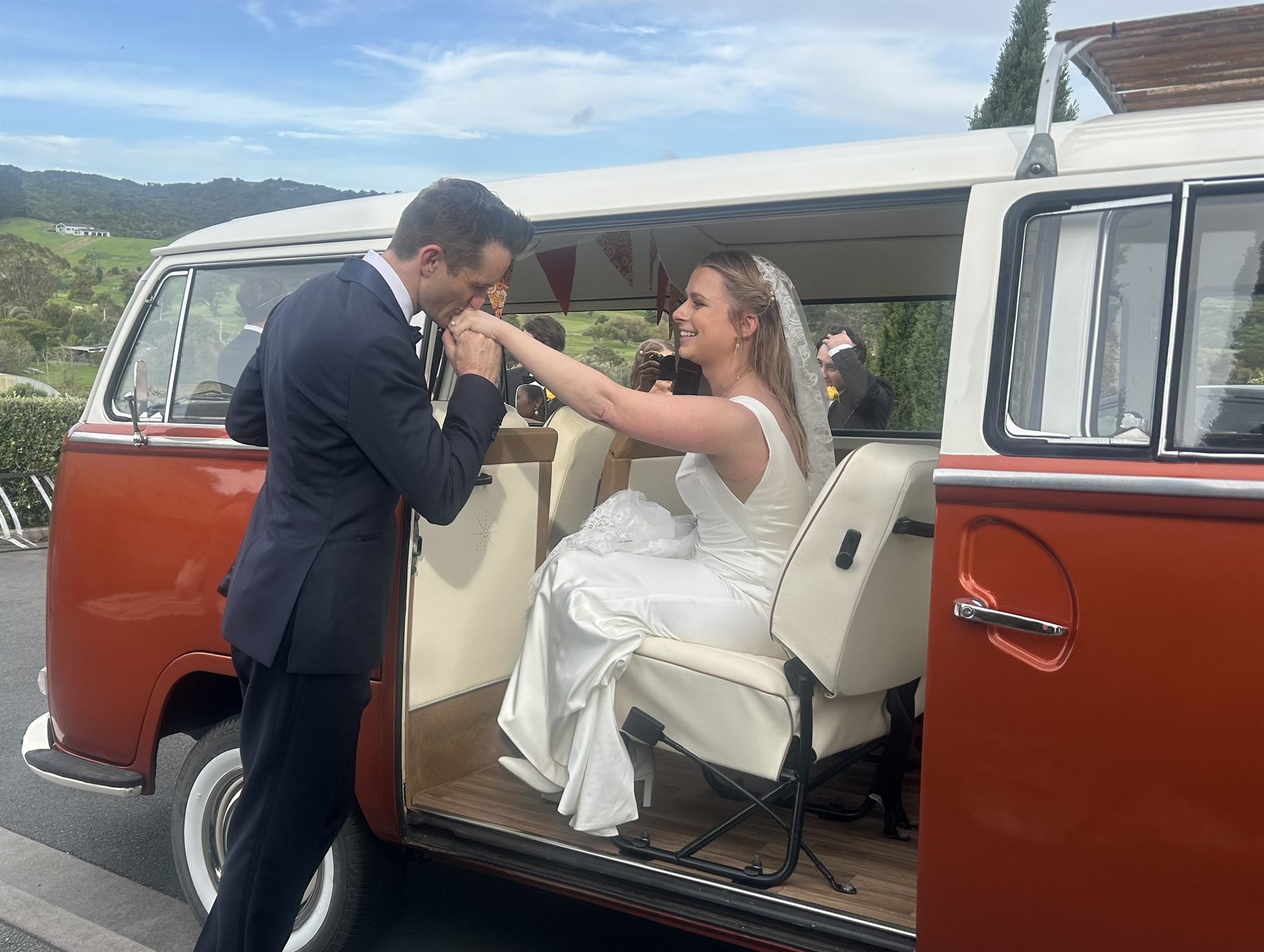 Groom kissing bride's hand at the door of Solana the 1969 Kombi van, Waiheke Island